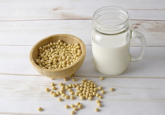 Soybeans in wooden bowl and glass of soy milk on white wood
