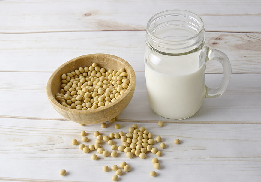 Soybeans in wooden bowl and glass of soy milk on white wood