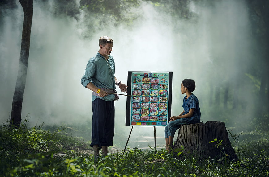 Teacher teaching alphabet to child in misty forest