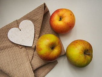 Three apples and wooden heart on brown napkin