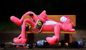 Pink Panther plush toy drunk on miniature bench with alcohol bottles