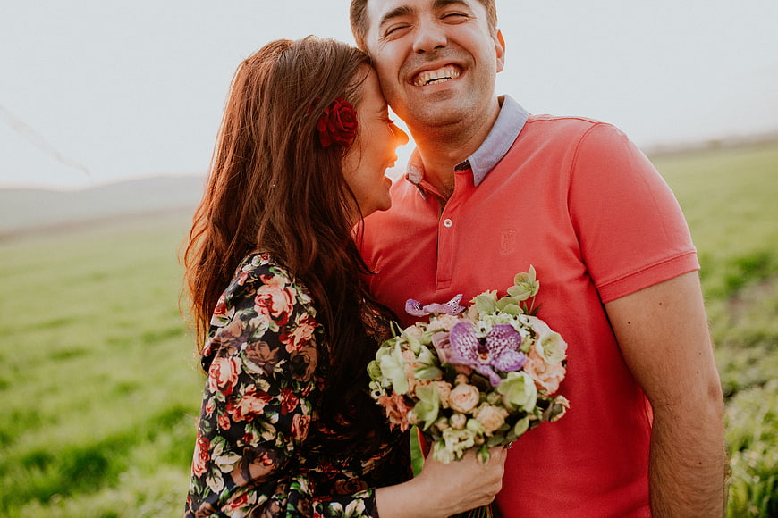 Happy couple laughing in field with bouquet