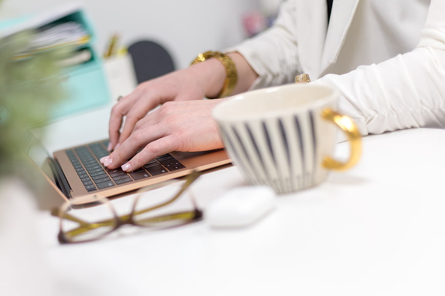 Woman Typing on Laptop with Coffee and Glasses on Desk