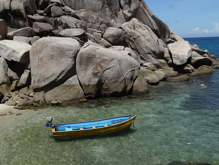 Yellow and blue boat anchored in clear tropical water near rocks