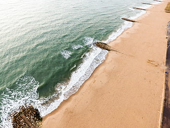 Aerial view of sandy beach with ocean waves and rock groynes