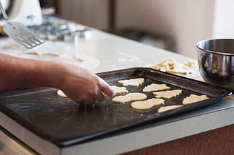 Hands placing cookie dough shapes on baking sheet
