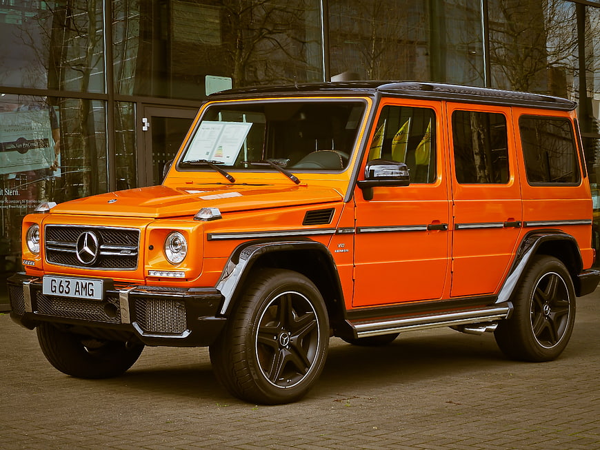 Orange Mercedes-Benz G63 AMG SUV Parked Before Glass Facade