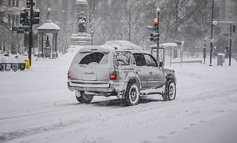 Snow covered SUV driving through heavy winter blizzard in city