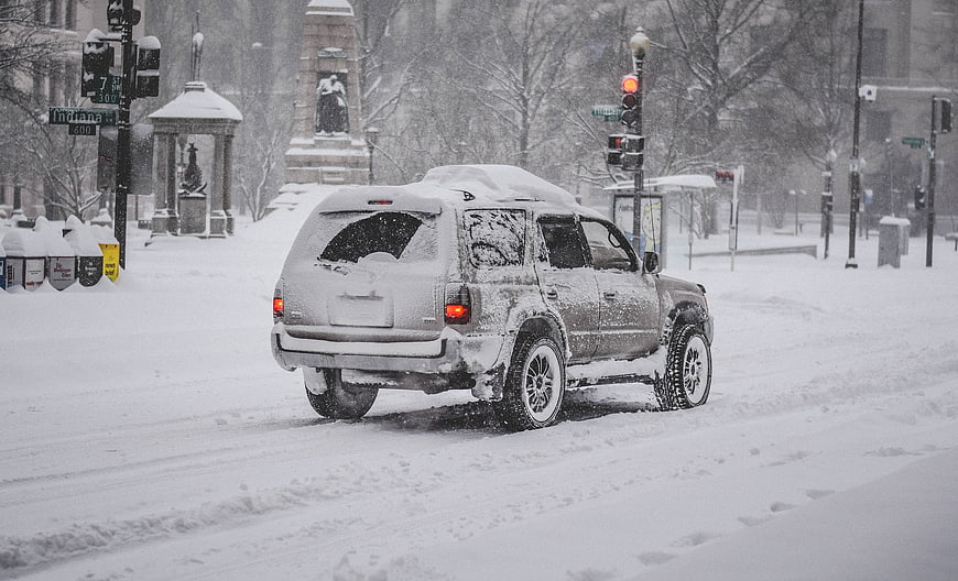Snow covered SUV driving through heavy winter blizzard in city