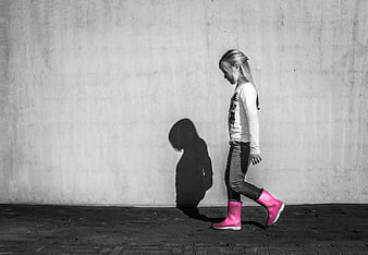 Little girl walking with pink boots against gray wall