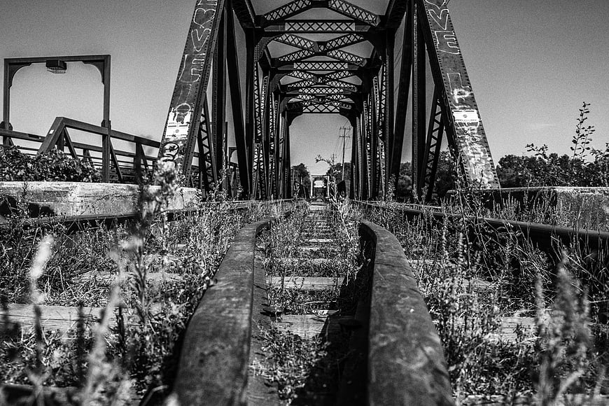 Abandoned Railway Bridge with Overgrown Tracks in Black and White