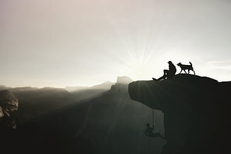 Silhouette of Climber and Dog on Mountain Cliff at Sunset