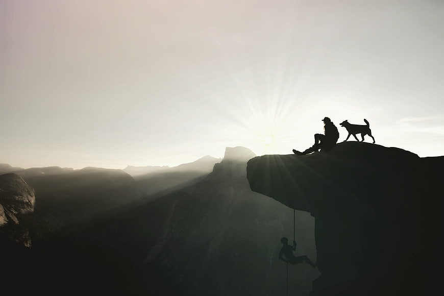 Silhouette of Climber and Dog on Mountain Cliff at Sunset