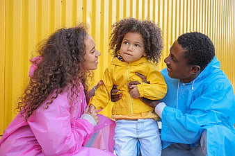 Happy Black Family in Colorful Raincoats Against Yellow Wall