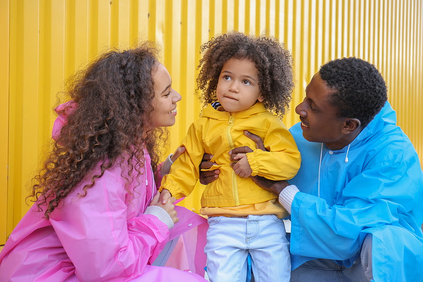 Happy Black Family in Colorful Raincoats Against Yellow Wall