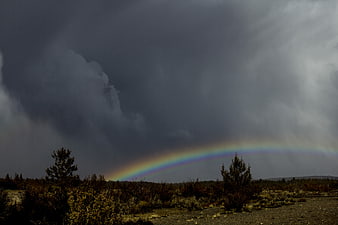 Vibrant Rainbow Arching Over Stormy Desert Landscape