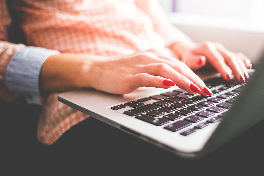 Close-up of woman typing on laptop with red nails