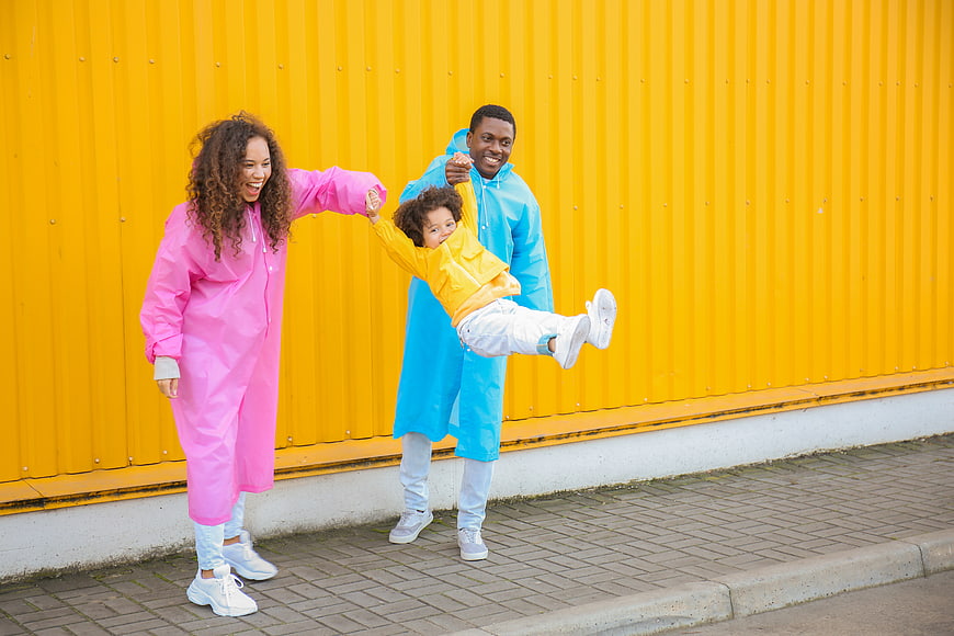 Happy family in colorful raincoats playing against yellow wall