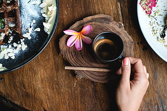 Top view of hand holding espresso cup with frangipani flower on wooden table