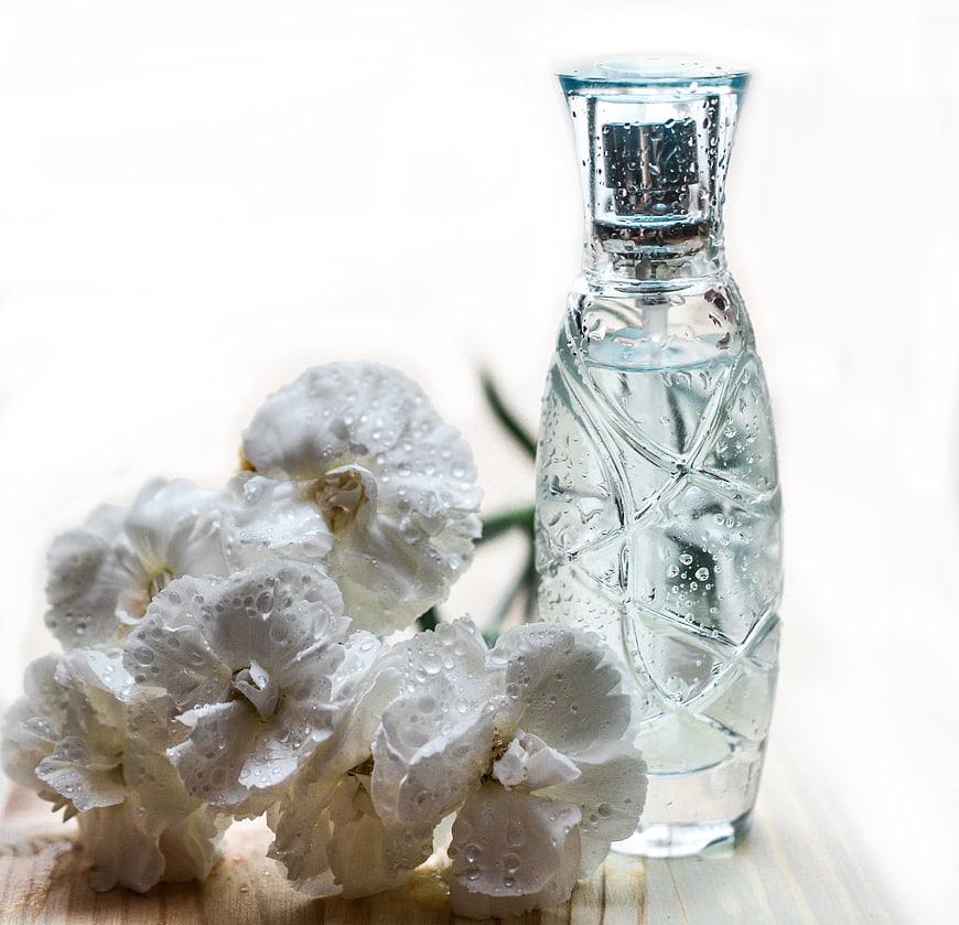 Glass perfume bottle with white flowers and water droplets