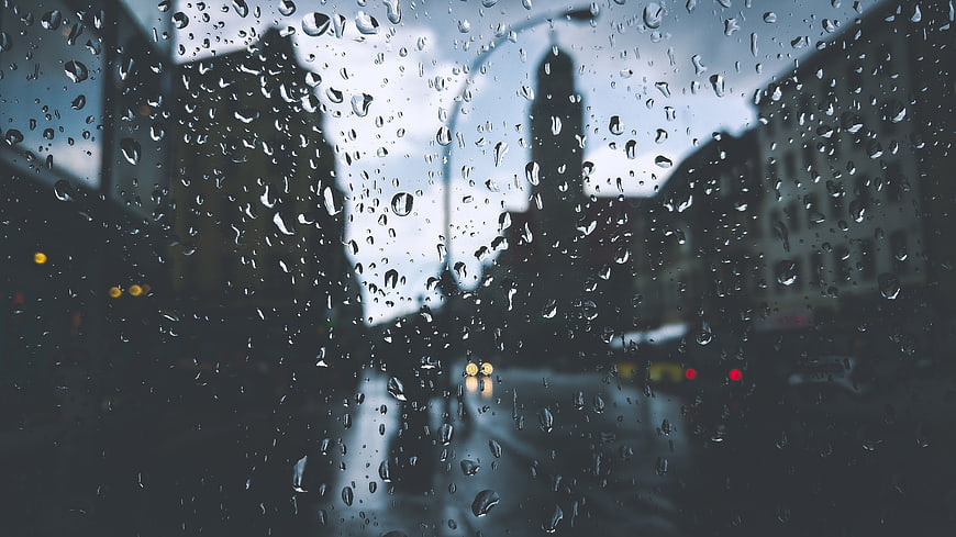 Raindrops on car windshield with blurred city street background