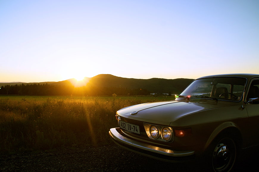 Vintage car parked in field at sunset with mountains