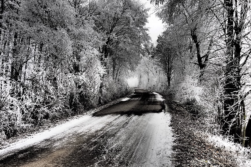 Black and white winter road through frosty forest
