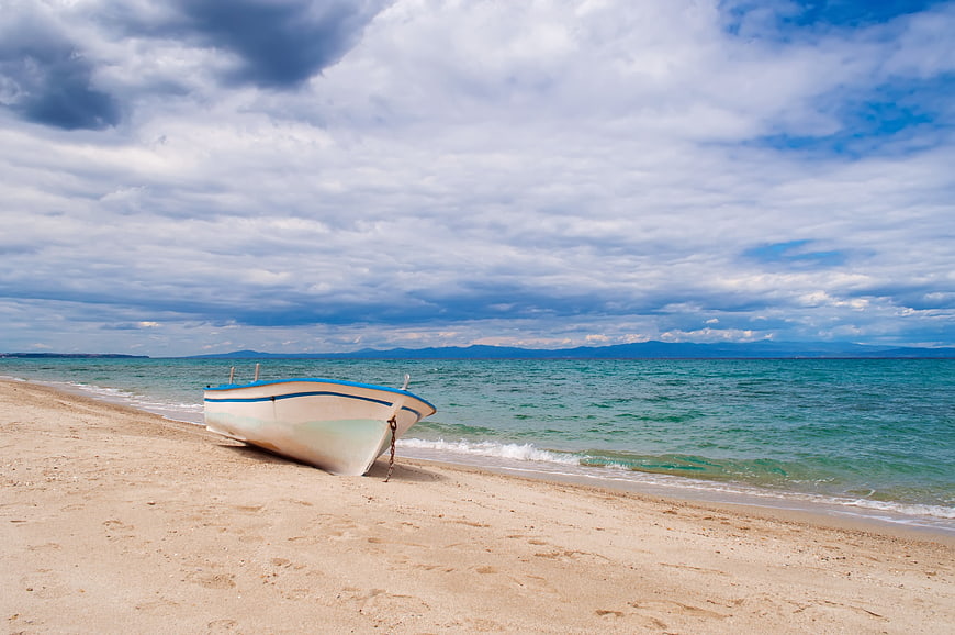 Small white boat resting on sandy beach with turquoise sea and dramatic cloudy sky