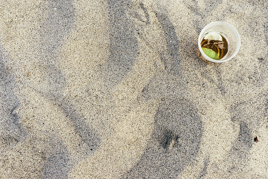 Plastic cup with cocktail on sandy beach background