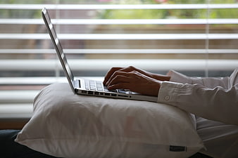 Hands typing on laptop on pillow by window