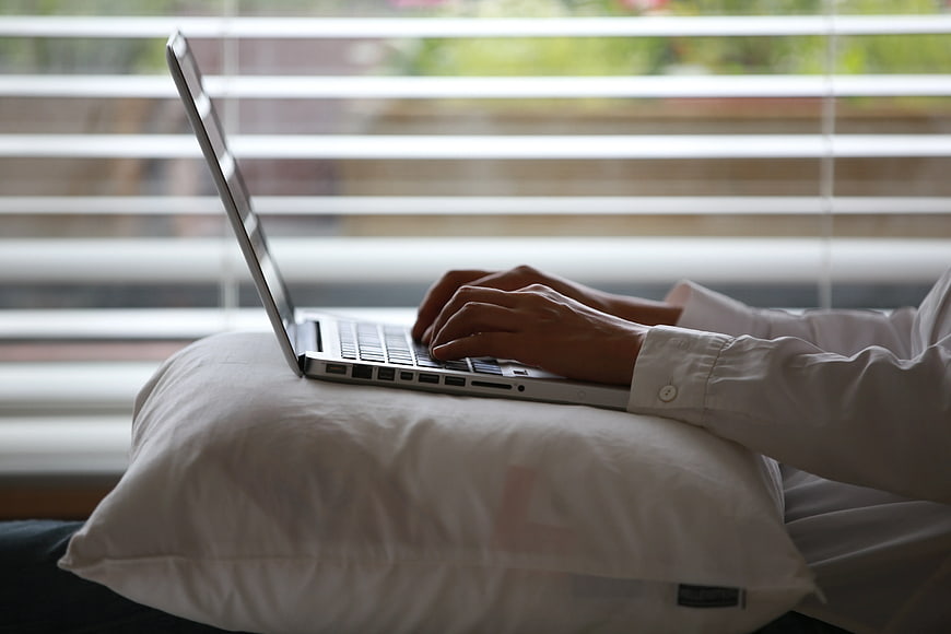 Hands typing on laptop on pillow by window