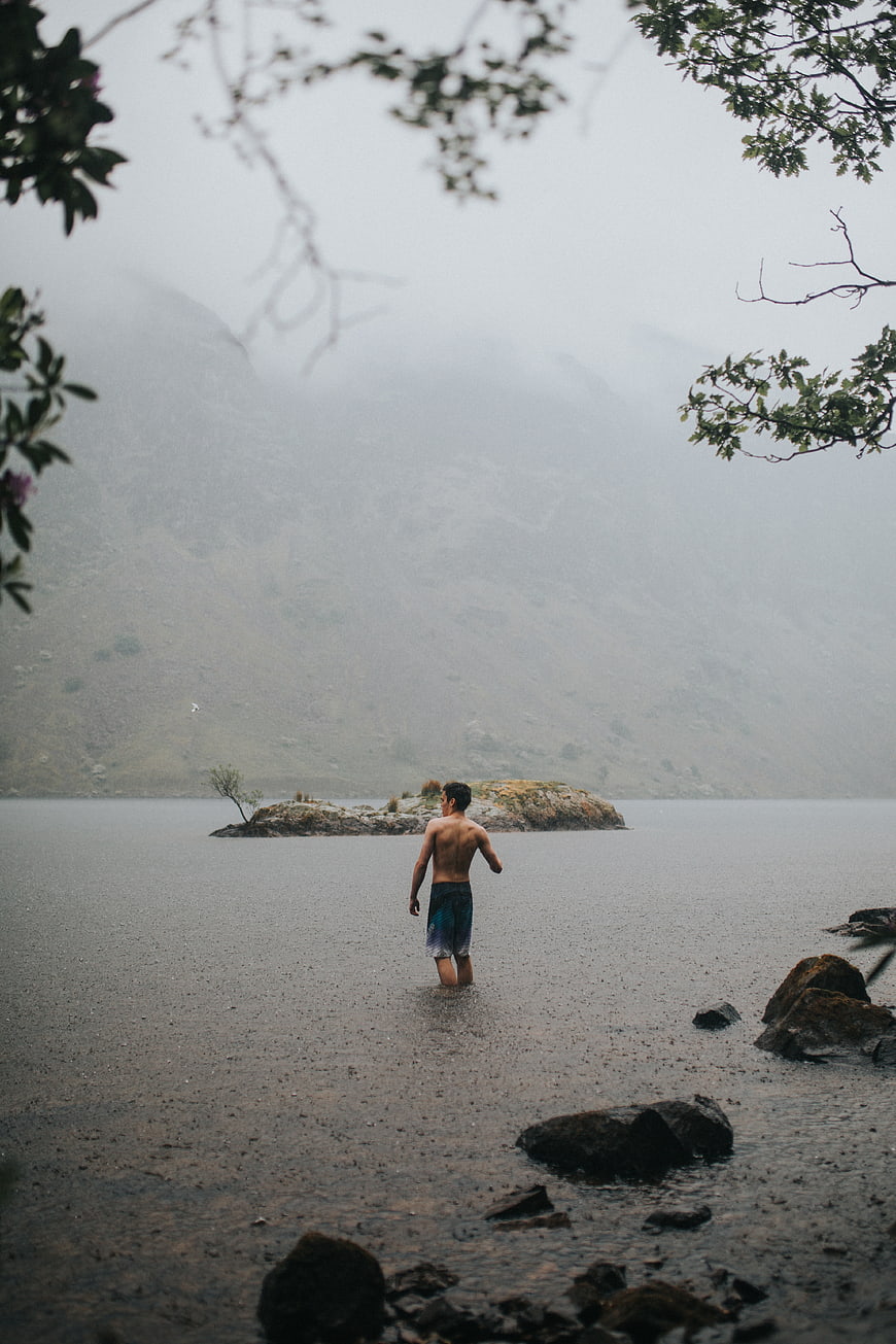 Man Walking in Rainy Lake with Foggy Mountains