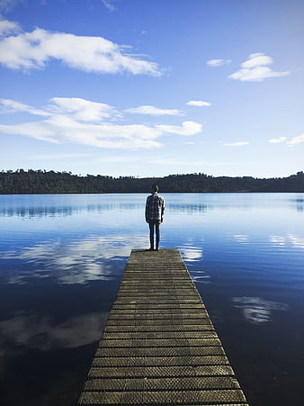 Man standing on wooden pier looking at calm lake
