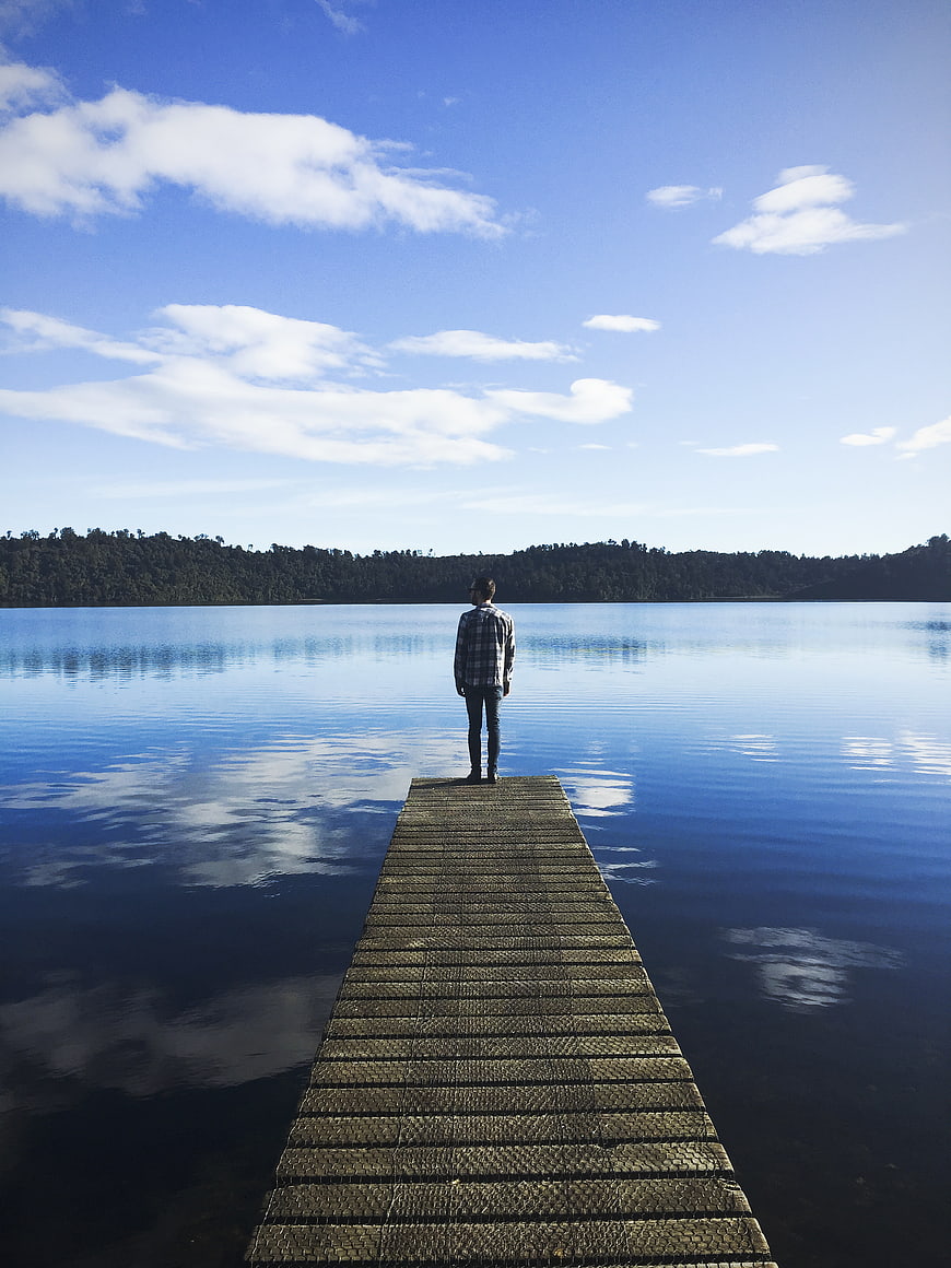 Man standing on wooden pier looking at calm lake