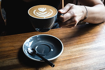 Hand holding cappuccino with latte art over wooden table