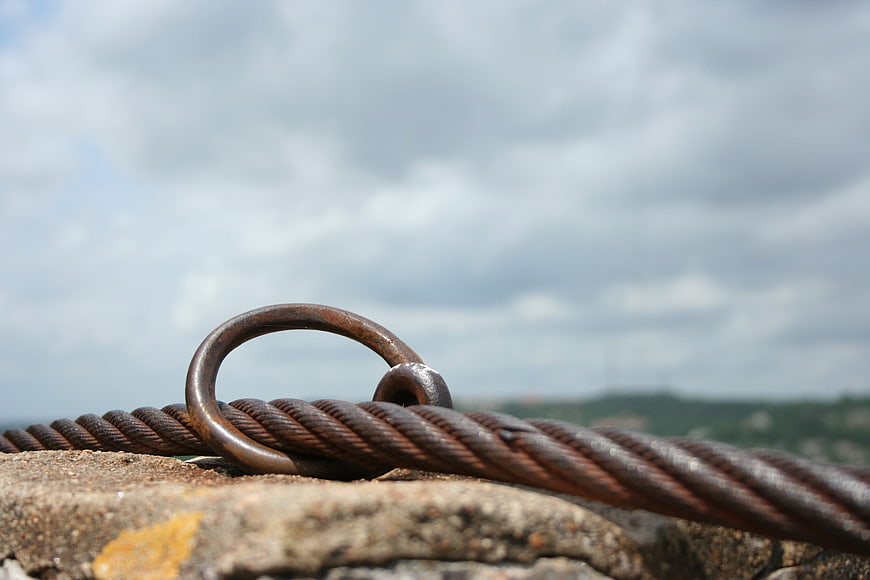 Close-up of rusty steel cable loop on rock against cloudy sky