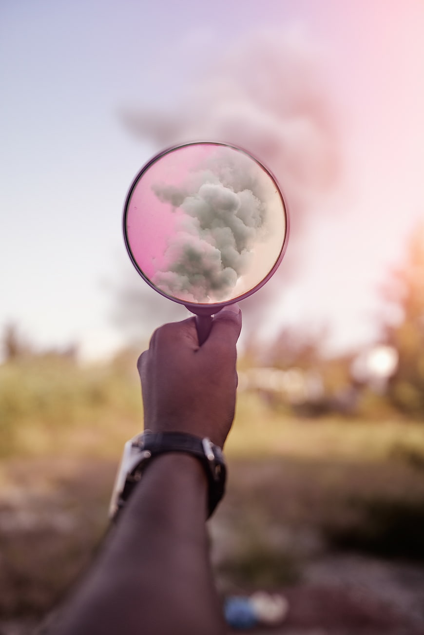 Hand holding mirror reflecting pink clouds in nature