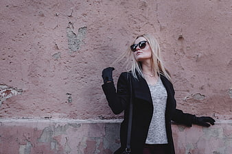 Blonde woman in sunglasses leaning against textured pink wall