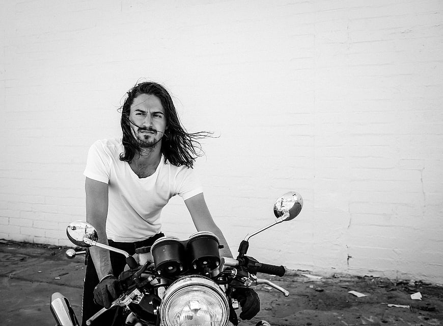 Man with Long Hair on Motorcycle Against White Wall