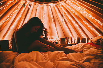 Woman sitting on bed in cozy yurt with fairy lights