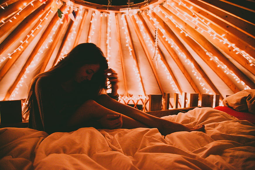 Woman sitting on bed in cozy yurt with fairy lights