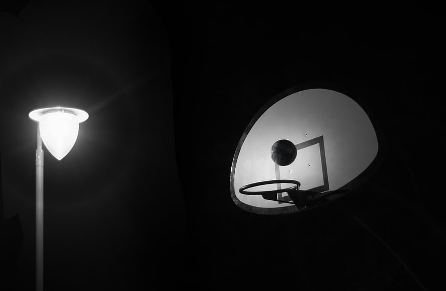 Black and white basketball hoop at night with street lamp