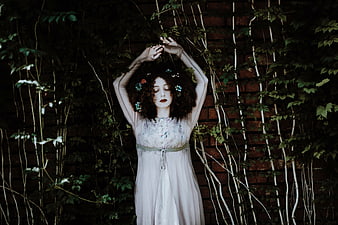 Woman in white dress with flower crown against ivy wall