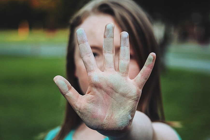 Girl holding up hand covered in colorful chalk paint
