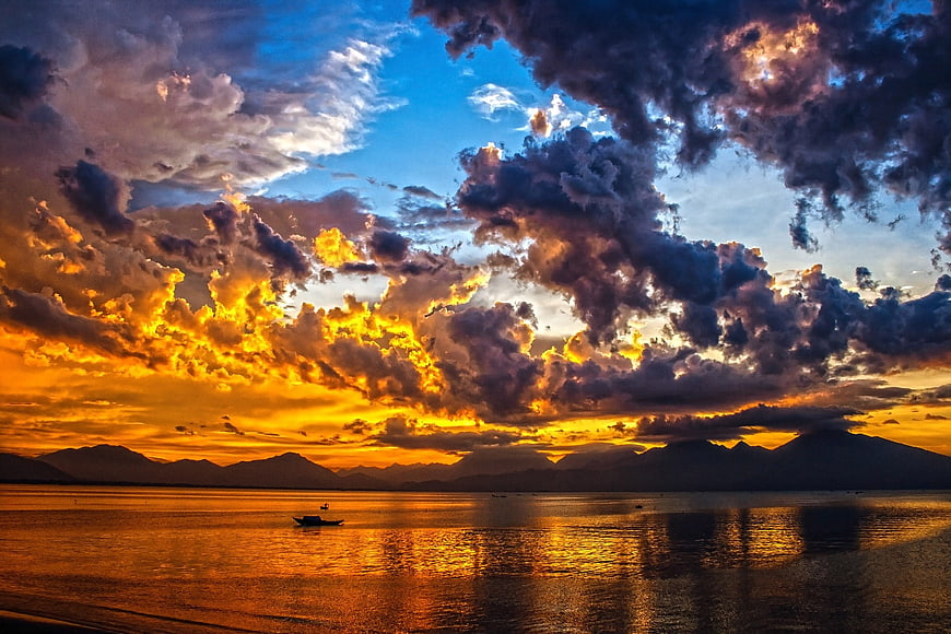 Dramatic Golden Sunset Over Ocean with Silhouette Mountains and Boat