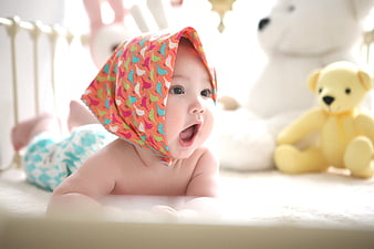 Baby Wearing Colorful Bird Patterned Hat In Nursery Bed With Stuffed Animals