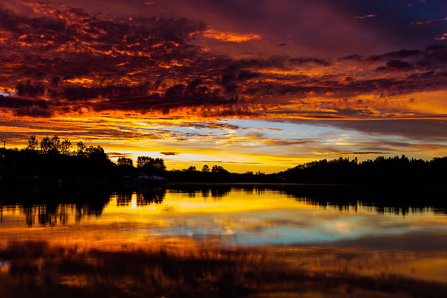 Dramatic fiery sunset over calm lake with tree silhouettes