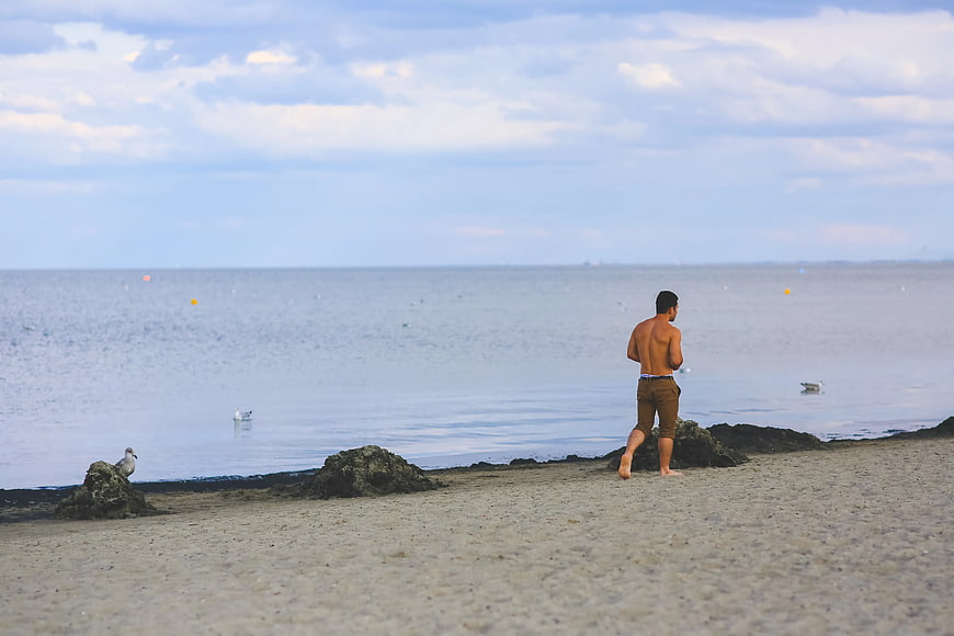 Shirtless man walking on sandy beach near calm ocean