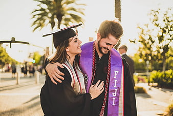 Happy Graduating Couple Hugging in Caps and Gowns
