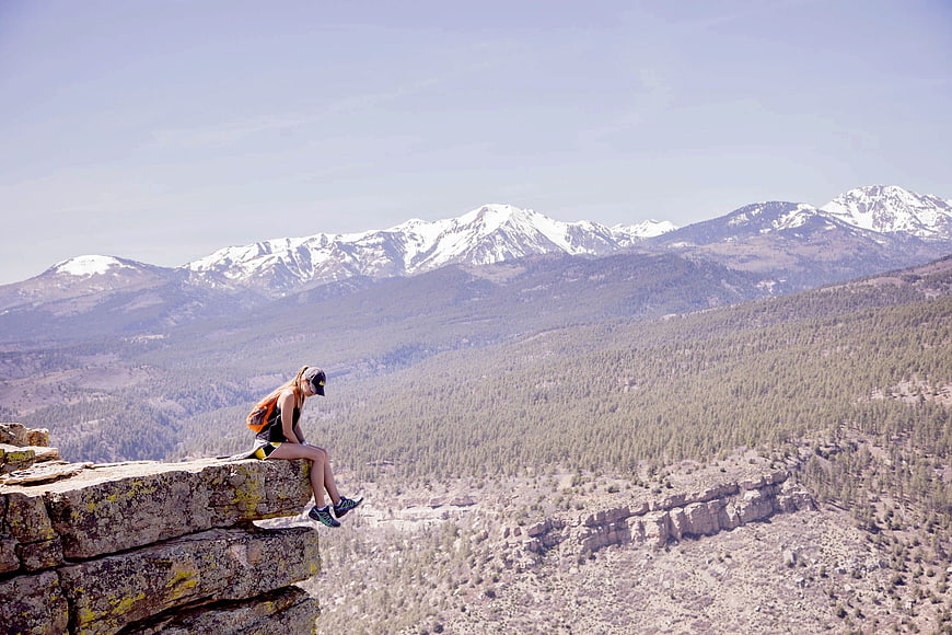 Woman hiker sitting on cliff edge overlooking snowy mountain range